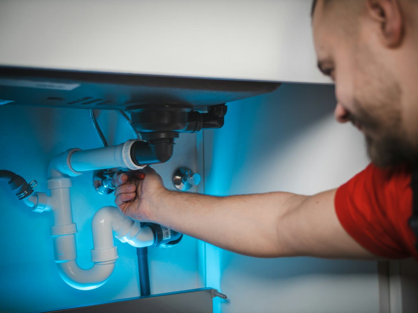A plumber tightening the pipes under a sink