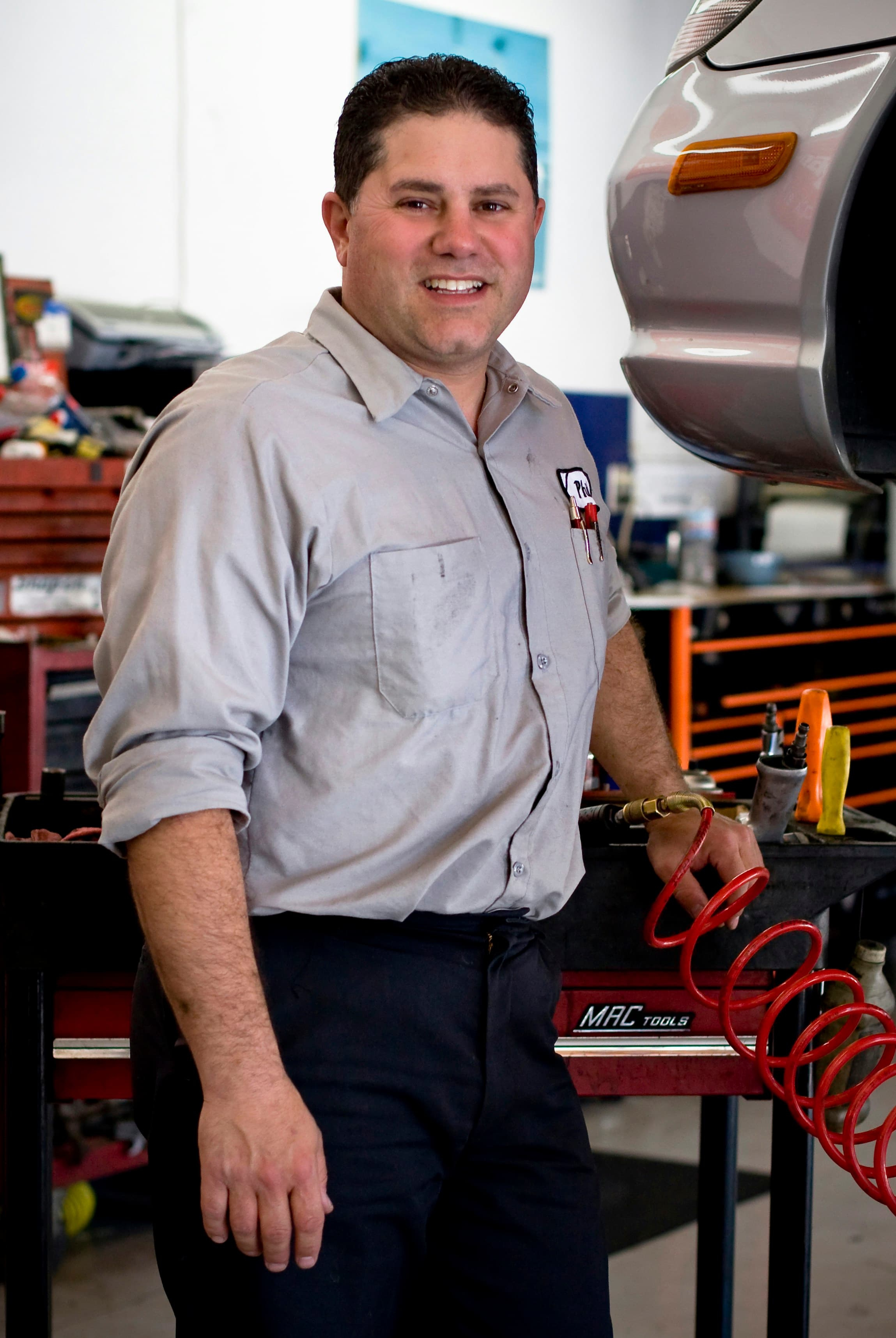 A shop owner in a work shirt smiling in his garage