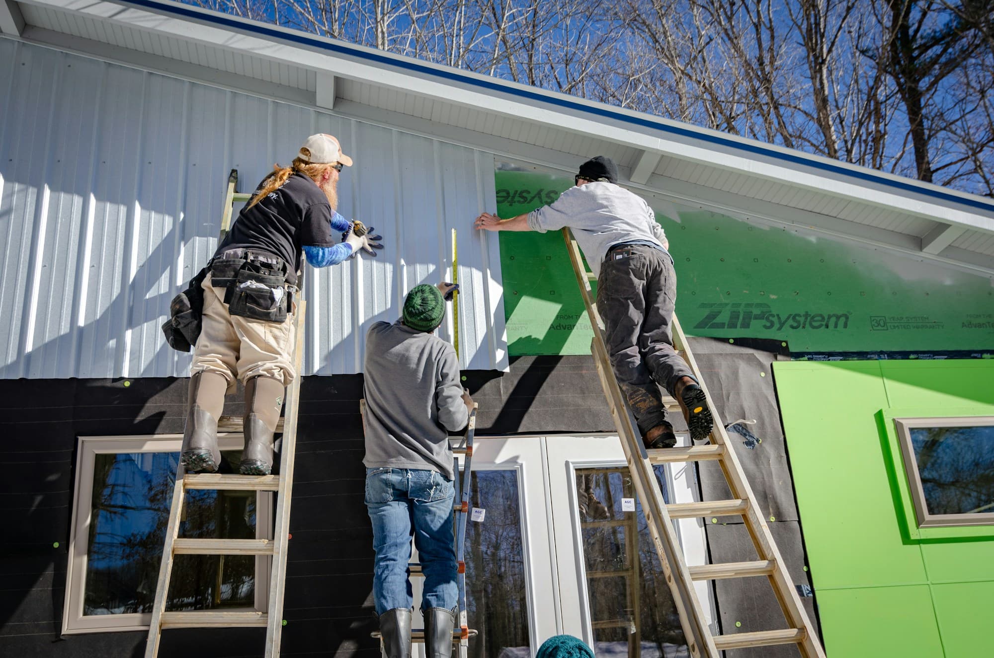 Three workers on ladders putting siding on a house