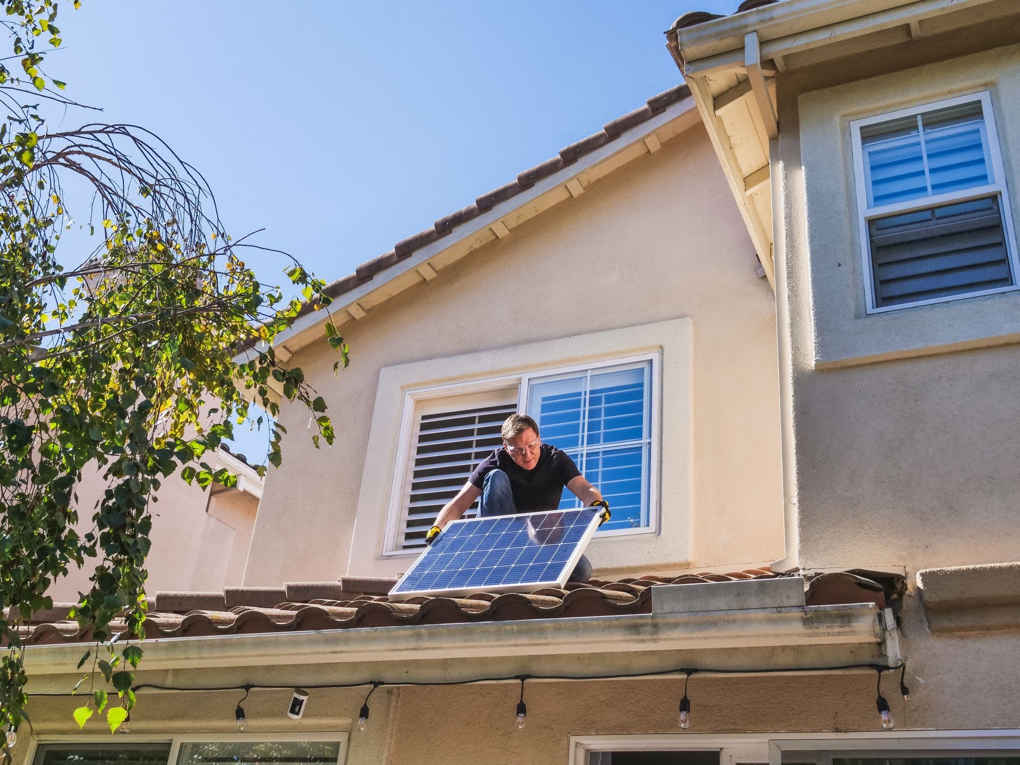 A technician carrying a solar panel across the roof of a house