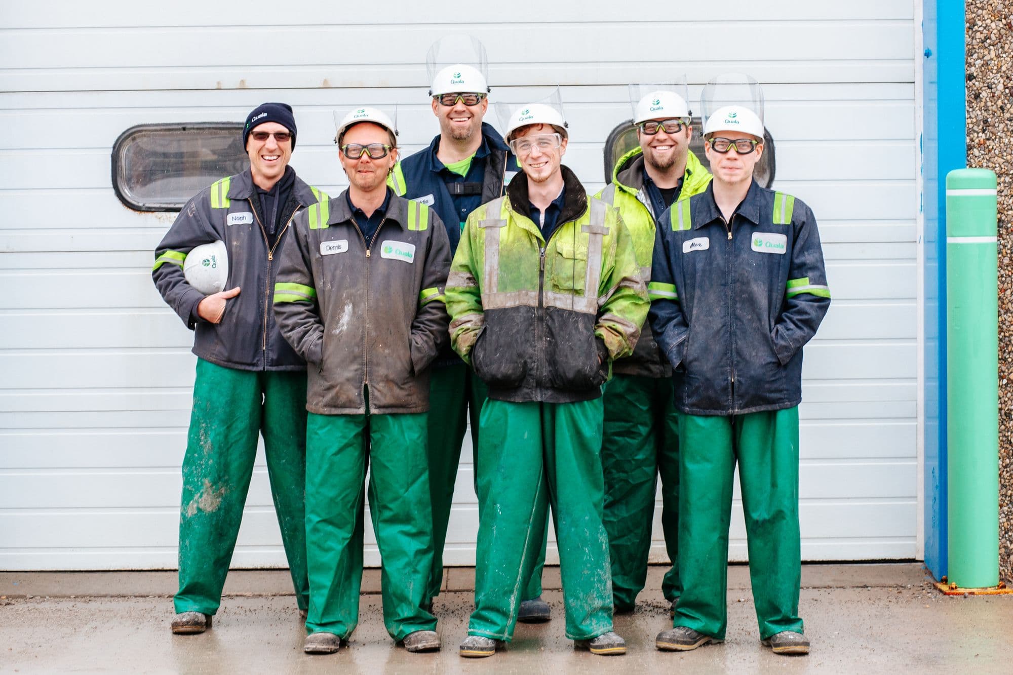 Six workers in matching uniforms and hard hats standing in front of a garage door