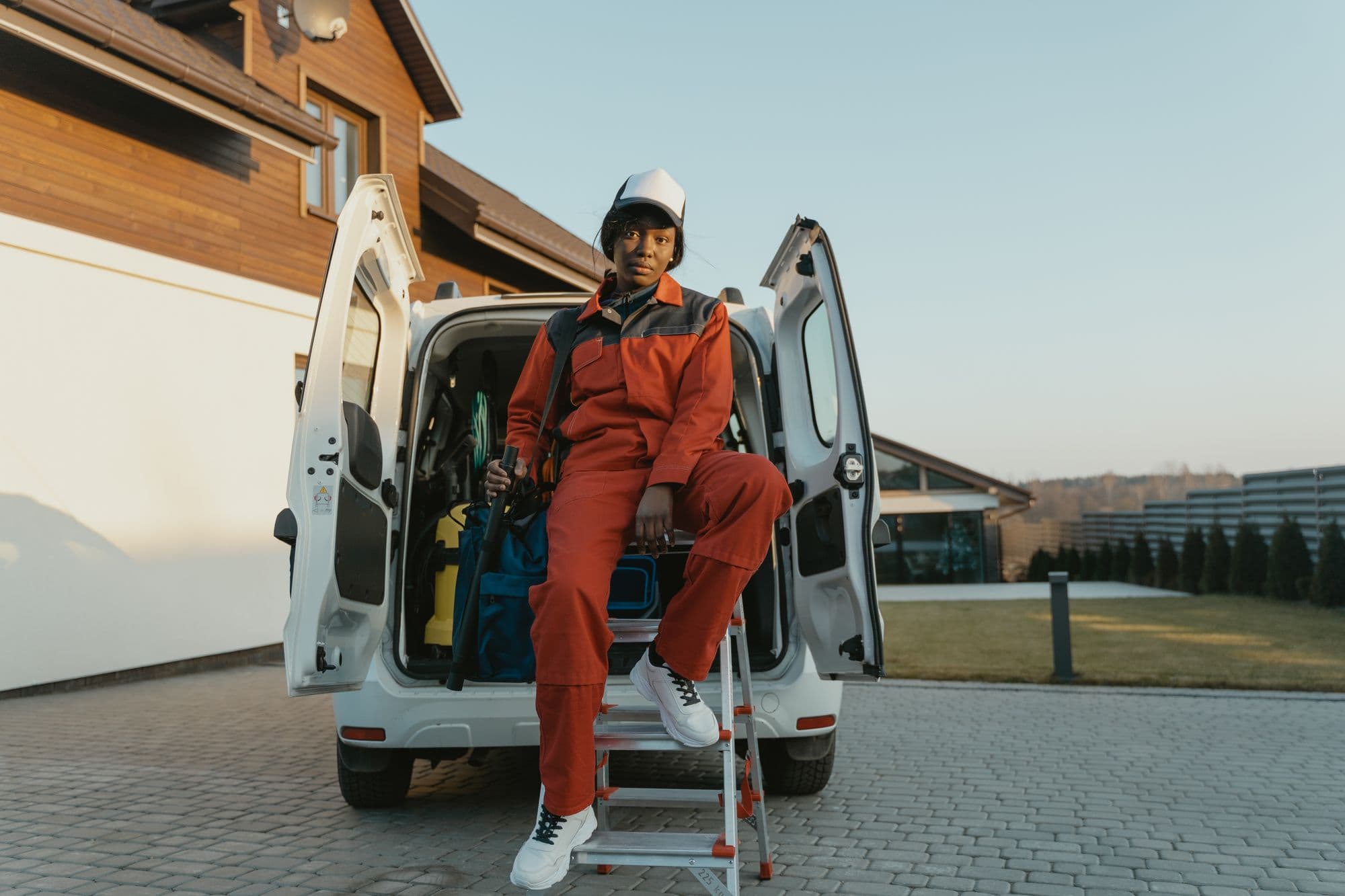 A worker in orange coveralls sitting on the step of an open work van in a driveway