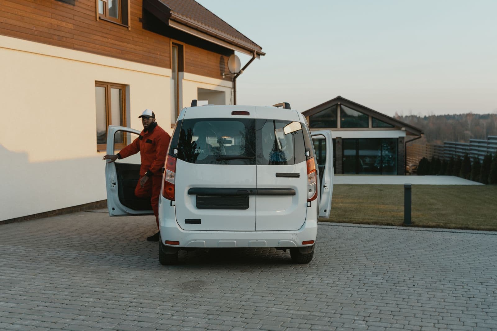 A technician in a red uniform getting out of a white work van parked in a home's driveway